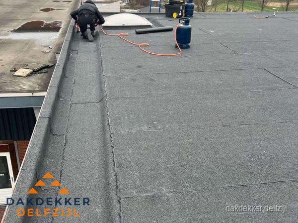 Dakdekker repareert bitumen dakbedekking op groot plat dak in Delfzijl