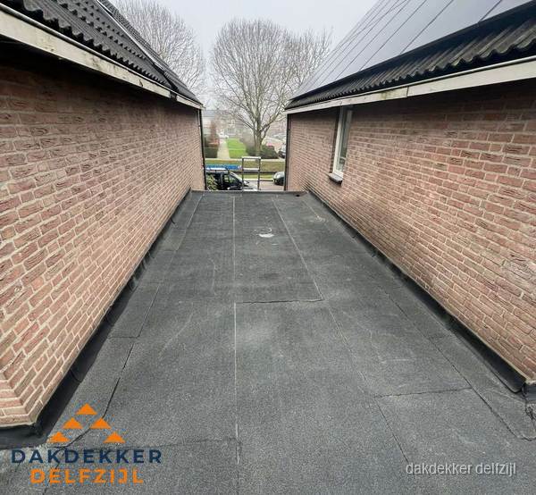 Plat dak met bitumen dakbedekking tussen bakstenen muren in Delfzijl Plat dak met bitumen dakbedekking tussen bakstenen muren in Delfzijl